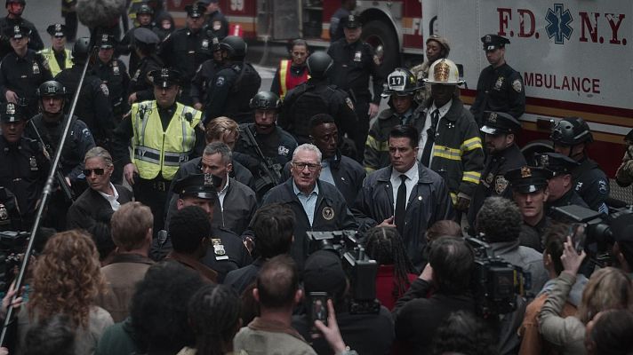 Robert De Niro, en el set de rodaje, viste chaqueta oscura y gafas.  La escena parece mostrar una situación de emergencia con bomberos, policías y una ambulancia.