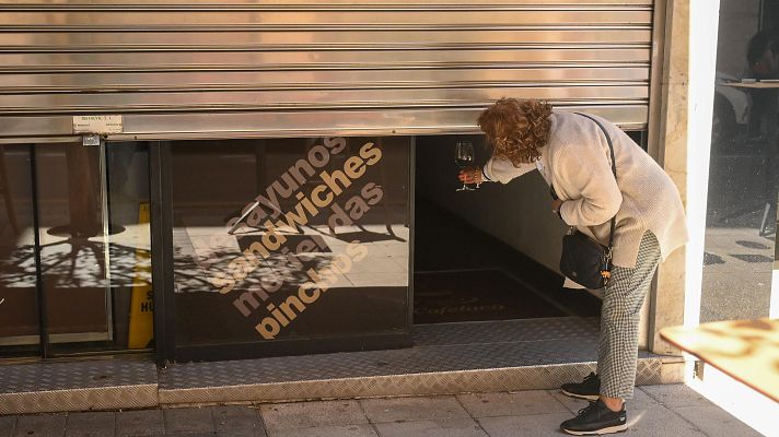 Mujer observa local con persiana semi-bajada anunciando desayunos, sandwiches y menú.  Posiblemente comprobando si está abierto tras un apagón.