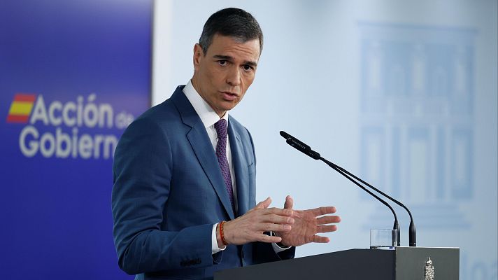El presidente español, en traje azul marino y corbata morada, realiza una declaración ante los medios, de pie tras un atril con el escudo nacional.
