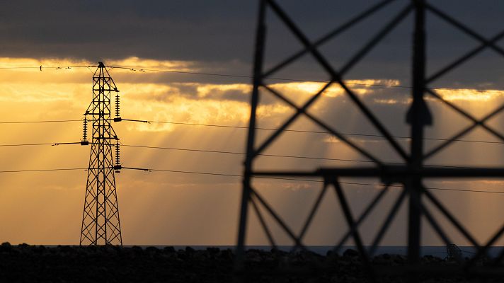Torre de alta tensión al atardecer, con estructura metálica en primer plano y mar al fondo.  Imagen evoca tranquilidad.