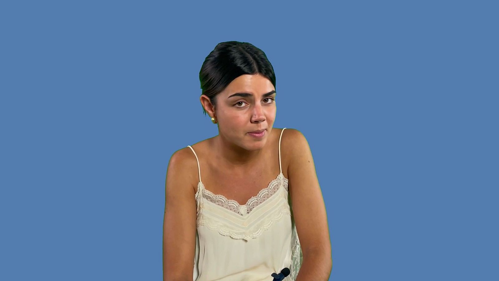 Mujer joven con cabello recogido y camiseta clara sobre fondo azul.  Imagen promocional o captura de pantalla.