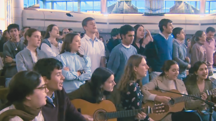 Jóvenes cantan y tocan guitarras en un encuentro religioso, mostrando emoción y un ambiente comunitario.