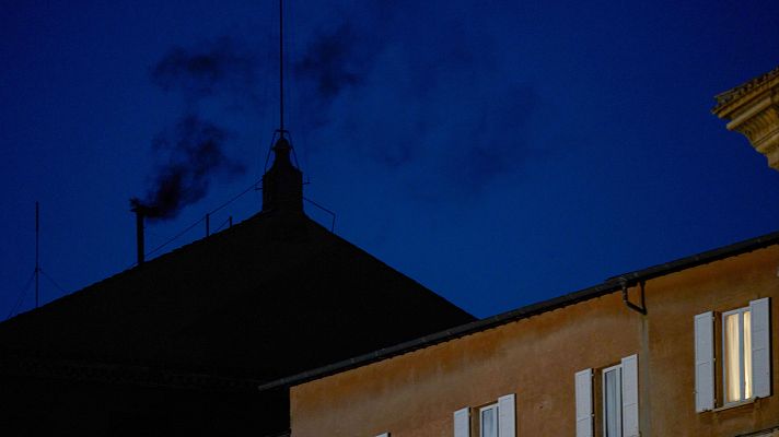 Humos negros nocturnos sobre el Vaticano indican que el cónclave papal continúa sin Papa elegido.  Se observa un edificio con una ventana iluminada.