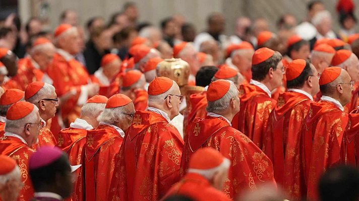 Numerosos cardenales, vestidos con capas rojas, esperan en un espacio concurrido.  La imagen sugiere un evento de gran importancia.