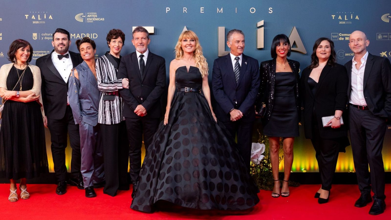 Grupo de nueve personas en gala posan en alfombra roja, con iluminación cálida y logos de patrocinadores.  Categoría: Laboratorio escénico.