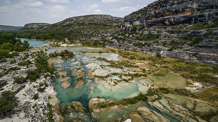 Río turquesa entre rocas, vegetación escasa y figura humana en una isla. Avance del documental \"Texas Corazón Salvaje\".