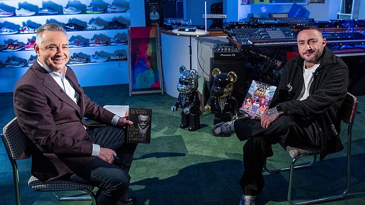 Entrevista en un espacio con zapatillas, equipos de música y figuras de osos. Un hombre sostiene un libro titulado \"DI NARDO\", el otro una revista \"Colegio XMYO\".