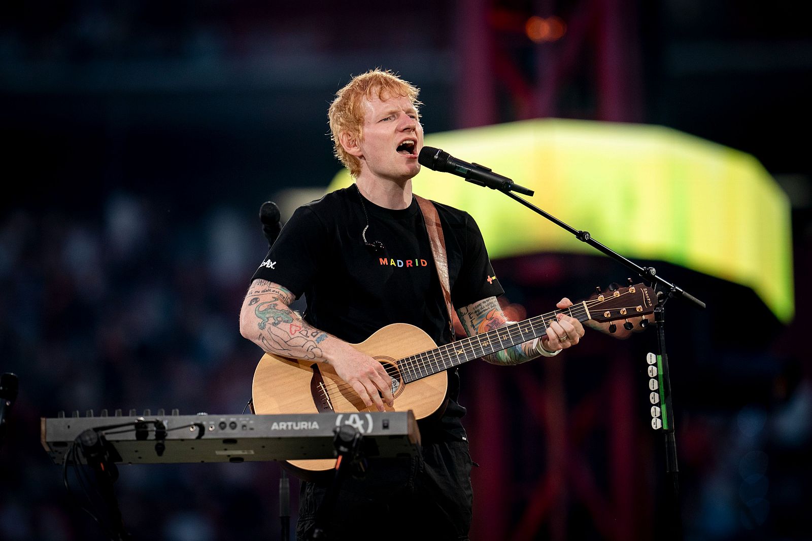 Concierto de Ed Sheeran en Madrid: guitarra acústica Arturia, camiseta con "MADRID" en arcoíris, público desenfocado.