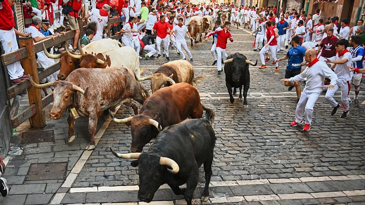 Multitud corriendo por una calle estrecha perseguida por toros durante un encierro.  La imagen captura la intensidad y el peligro del evento.