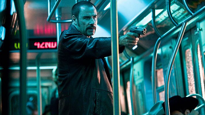 John Travolta, con pistola en mano, en un vagón de metro con iluminación azulada.  Su expresión seria refleja la tensión del momento.