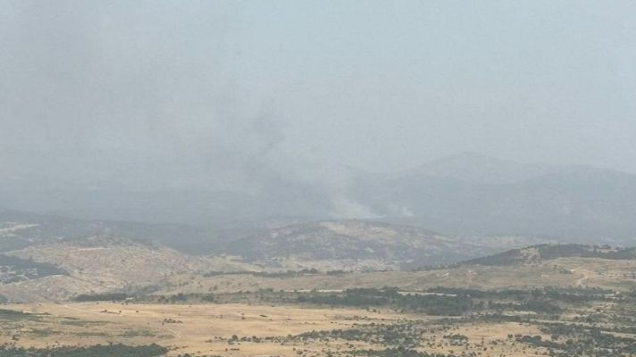 Imagen aérea de un incendio forestal en zona montañosa, con abundante humo gris.  El terreno dificulta la extinción.