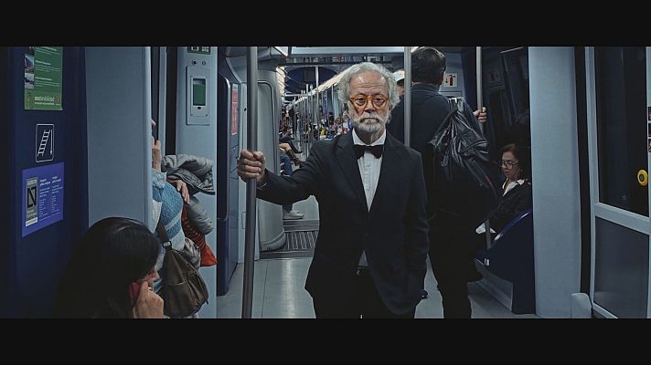 Hombre con esmoquin y pajarita en transporte público, posiblemente durante un festival. Otros pasajeros viajan en el mismo vagón.