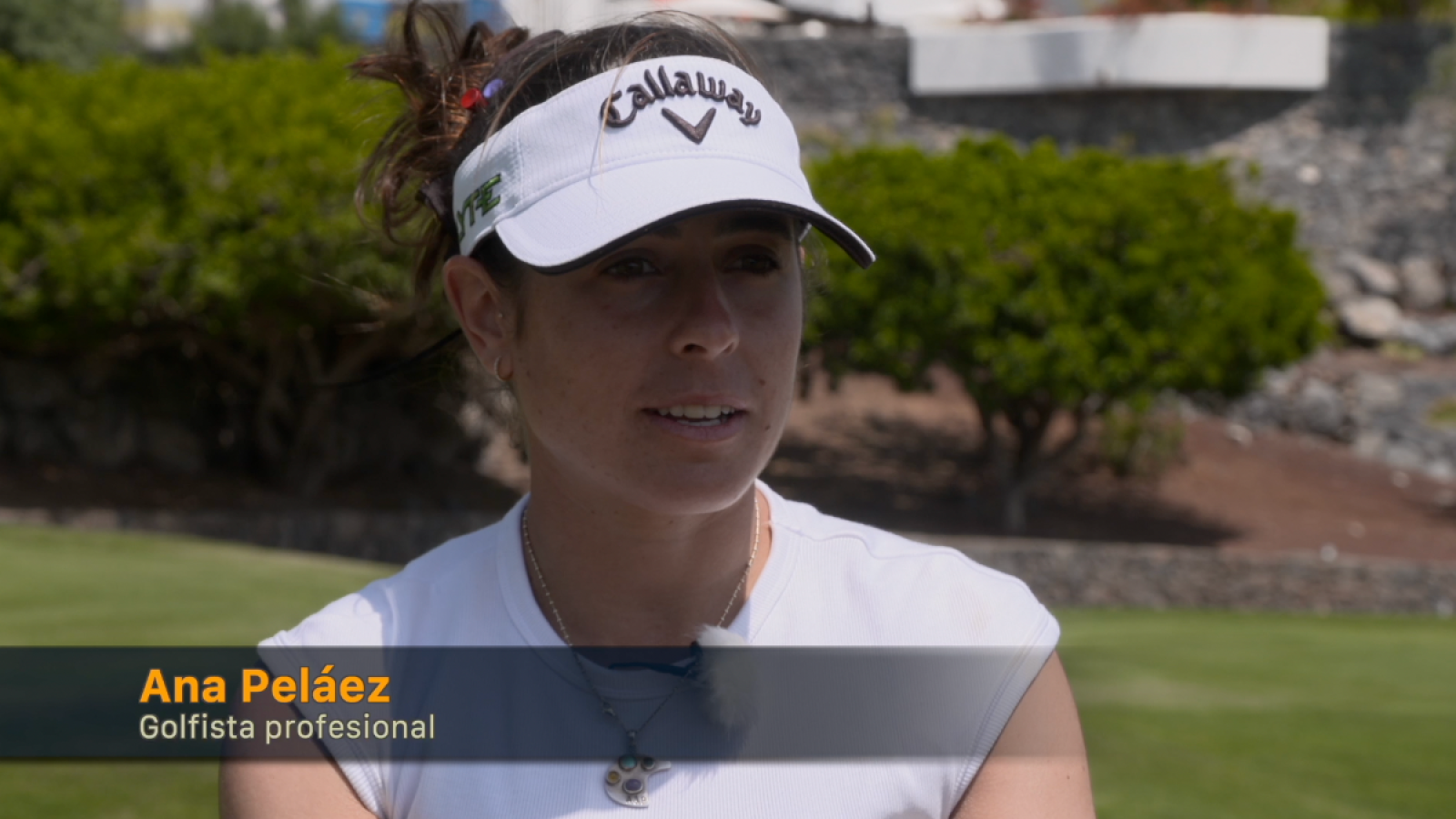 Entrevista a una golfista con visera blanca y camiseta blanca, en un entorno que parece un campo de golf.  Pelo recogido y collar visible.