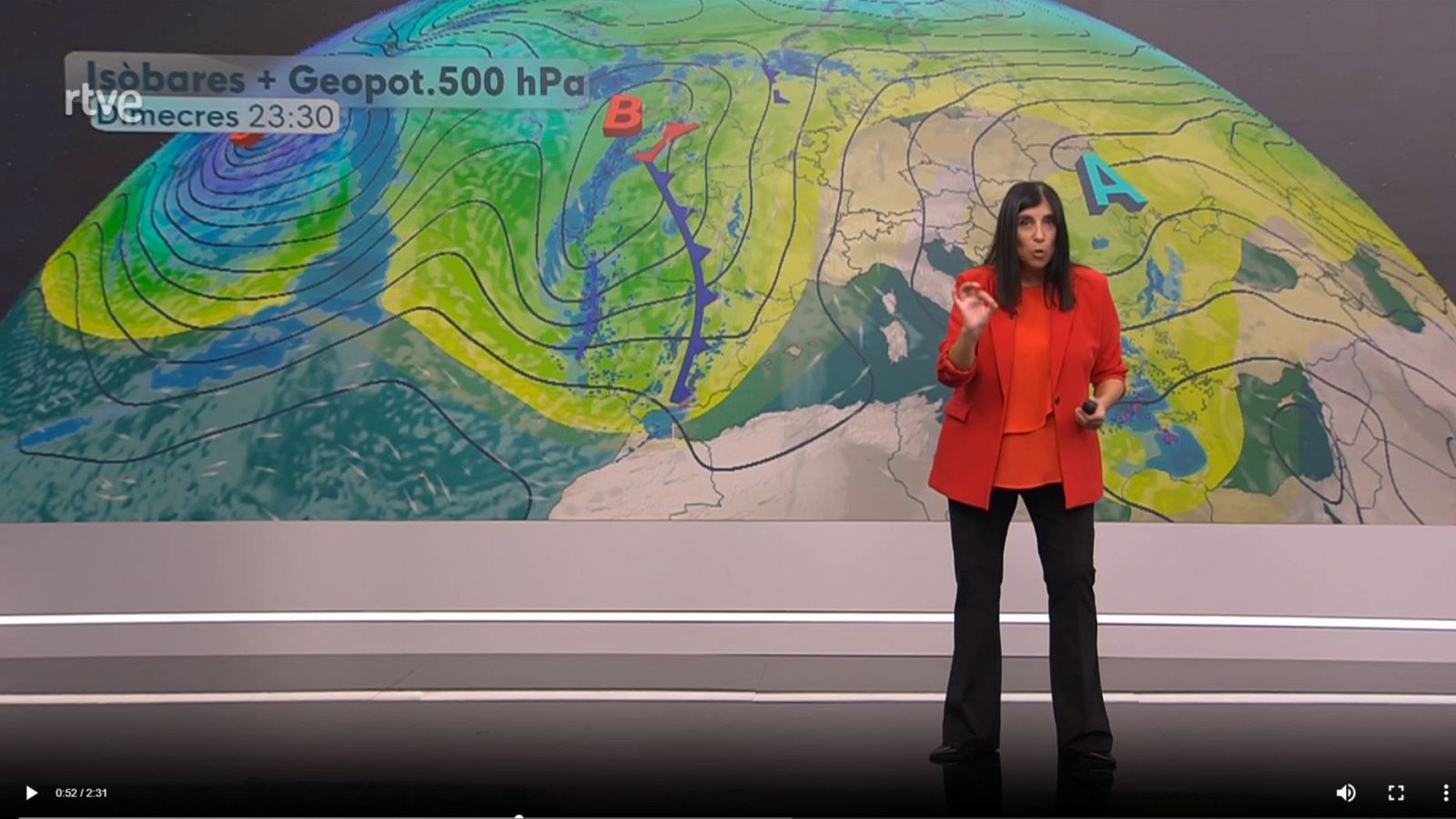Una mujer presenta el pronóstico del tiempo frente a un mapa que muestra isobaras y el geo potencial. Viste una blusa naranja y chaqueta roja, y gesticula con la mano derecha. En el mapa se lee "Isòbares + Geopot. 500 hPa" y la hora "Dimecres 23:30".