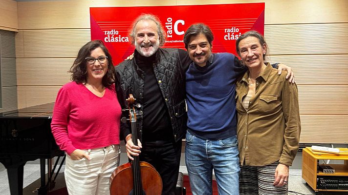 Cuatro personas sonríen en un estudio de radio, con un piano de cola y un panel rojo de fondo. Un hombre con un violonchelo, posiblemente José el Marqués, y una mujer con gafas destacan en la imagen.
