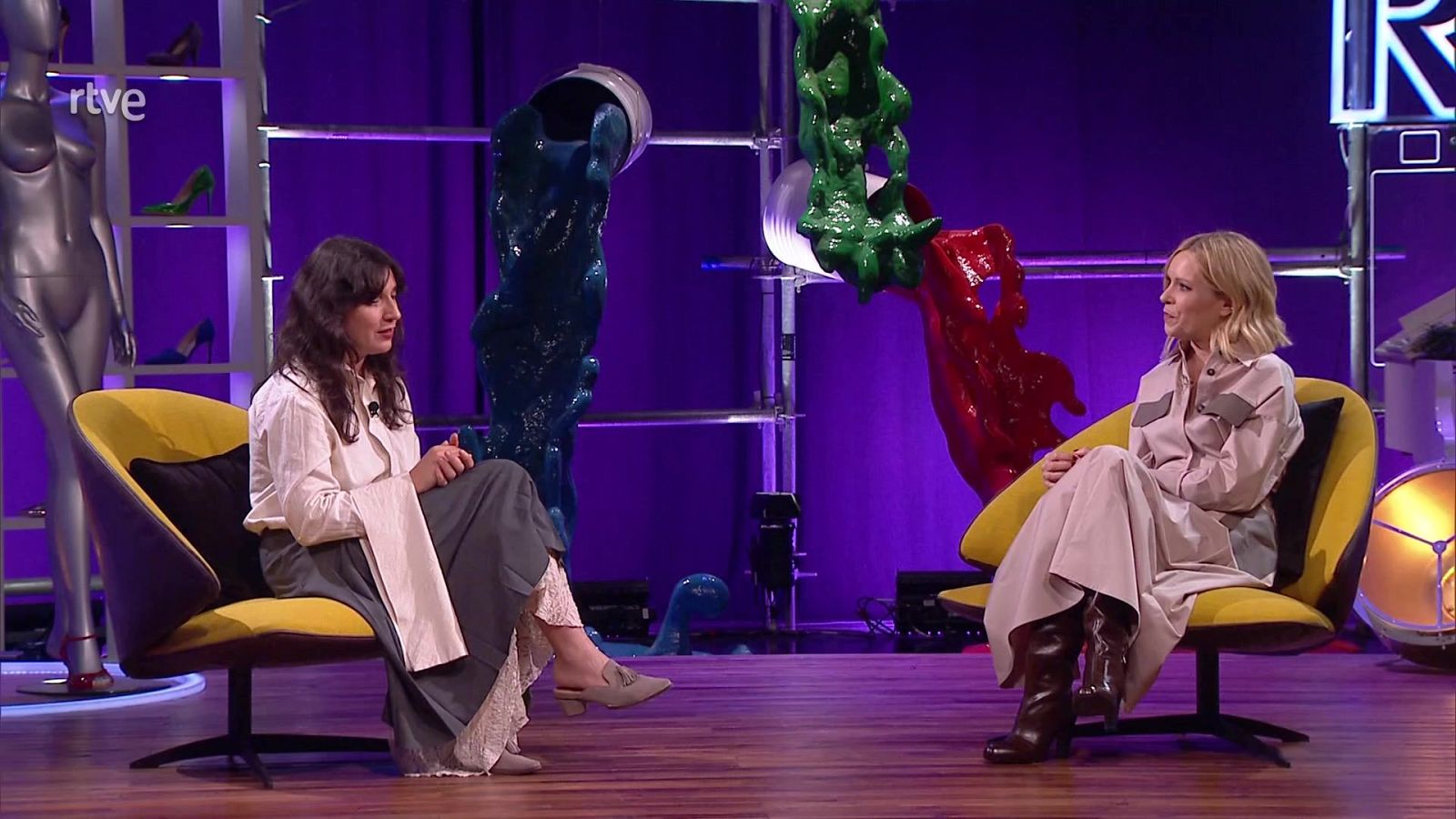 Dos mujeres participan en un programa de televisión en un estudio con fondo morado y elementos artísticos. Se distinguen los textos "lorena alvarez" y "Culturas 2", junto al logo de RTVE.