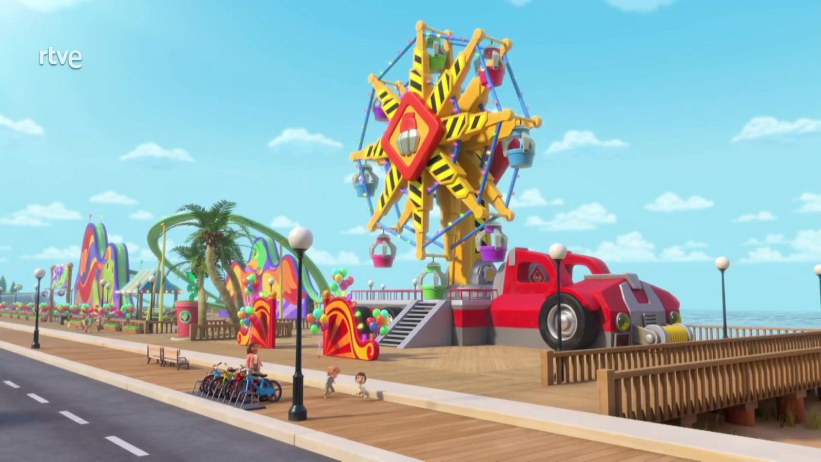 Un parque de atracciones costero se muestra en un día soleado, con una gran noria amarilla y cabinas de colores como elemento central, junto a un paseo marítimo con personas y el mar de fondo.