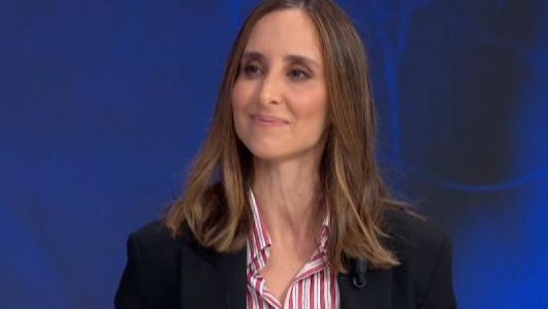 Julia Varela, con camisa a rayas y chaqueta oscura, posa frente a un fondo azul uniforme, con el cabello peinado con ondas suaves.