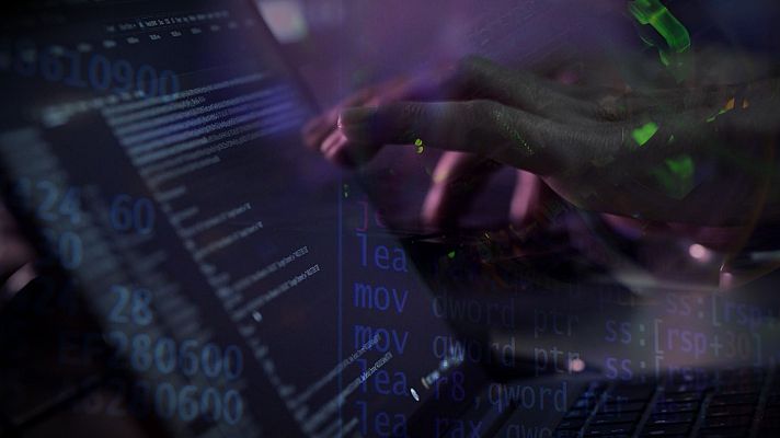 Un ordenador portátil muestra código informático en tonos azules y blancos, con unas manos tecleando sobre el teclado. La iluminación morada crea una atmósfera de misterio.