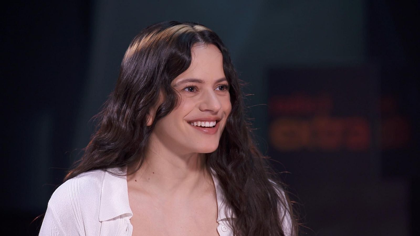 Una mujer sonríe a la cámara, con el pelo largo y castaño oscuro, destacando un mechón rubio. Lleva una camisa blanca.