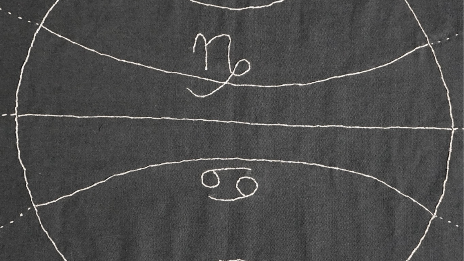 Un bordado abstracto en blanco sobre fondo oscuro muestra los símbolos astrológicos de Cáncer y Capricornio, atravesados por líneas blancas que sugieren una esfera dividida.