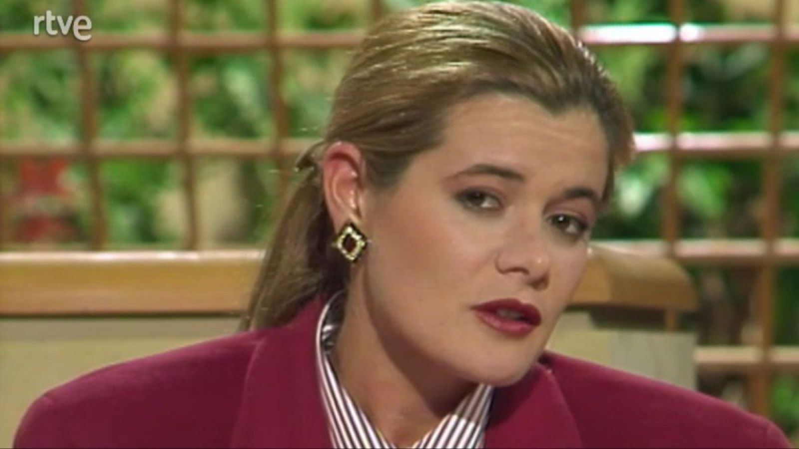 Elena Ochoa, psicóloga y sexóloga, en un plató de RTVE con chaqueta fucsia y camisa de rayas. Primer plano con maquillaje y pendiente.