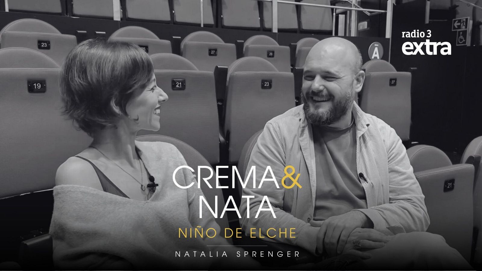 En una sala con asientos numerados, una mujer con vestido y chal sonríe junto a un hombre con barba y camiseta. El texto "CREMA & NATA" destaca en la parte inferior, junto a los nombres "NIÑO DE ELCHE" y "NATALIA SPRENGER".