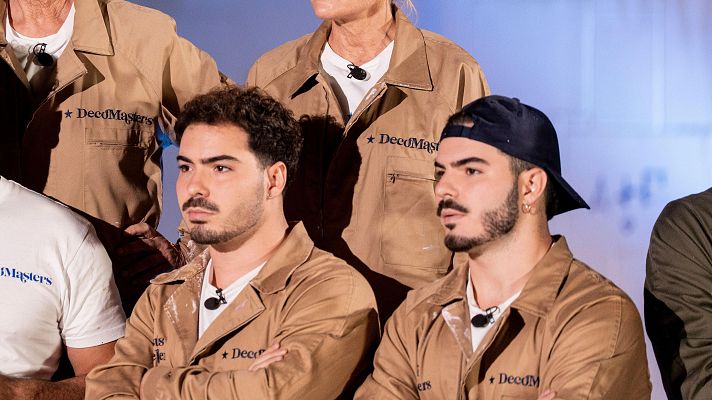 Dos hombres jóvenes, presumiblemente Gemeliers, posan con ropa de trabajo color café con el logo \"Decomasters\". Uno de ellos lleva una gorra oscura, y se ven otras personas con la misma vestimenta.