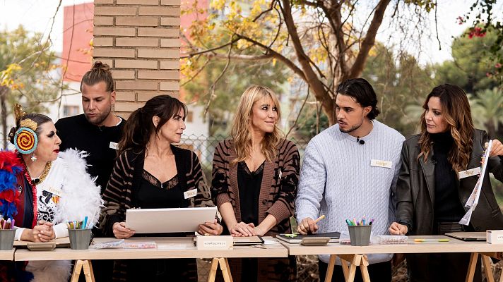Seis individuos se encuentran en una mesa exterior, destacando dos mujeres con chaquetas y blusas negras, una de ellas sosteniendo un papel. En la mesa hay materiales de dibujo y escritura.