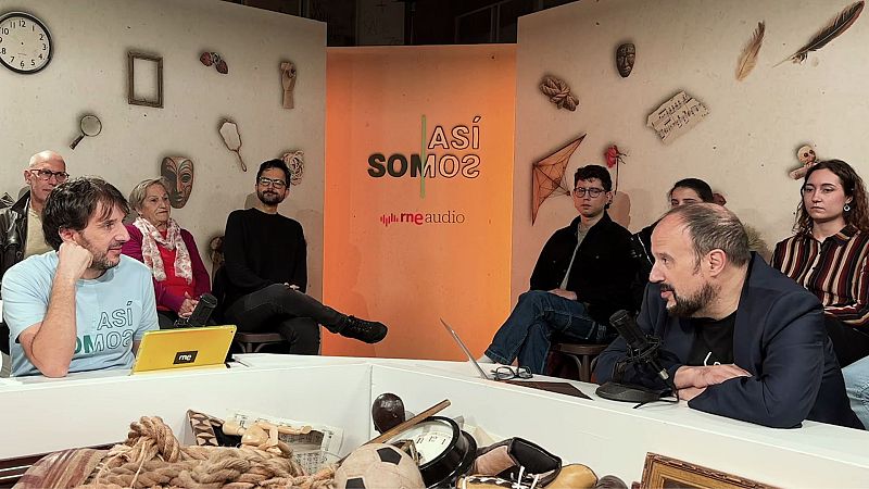 Un grupo de personas se encuentra en un estudio televisivo, posiblemente grabando un programa. Se observan varios individuos sentados alrededor de una mesa con diversos objetos, como un balón de fútbol y un marco de fotos.