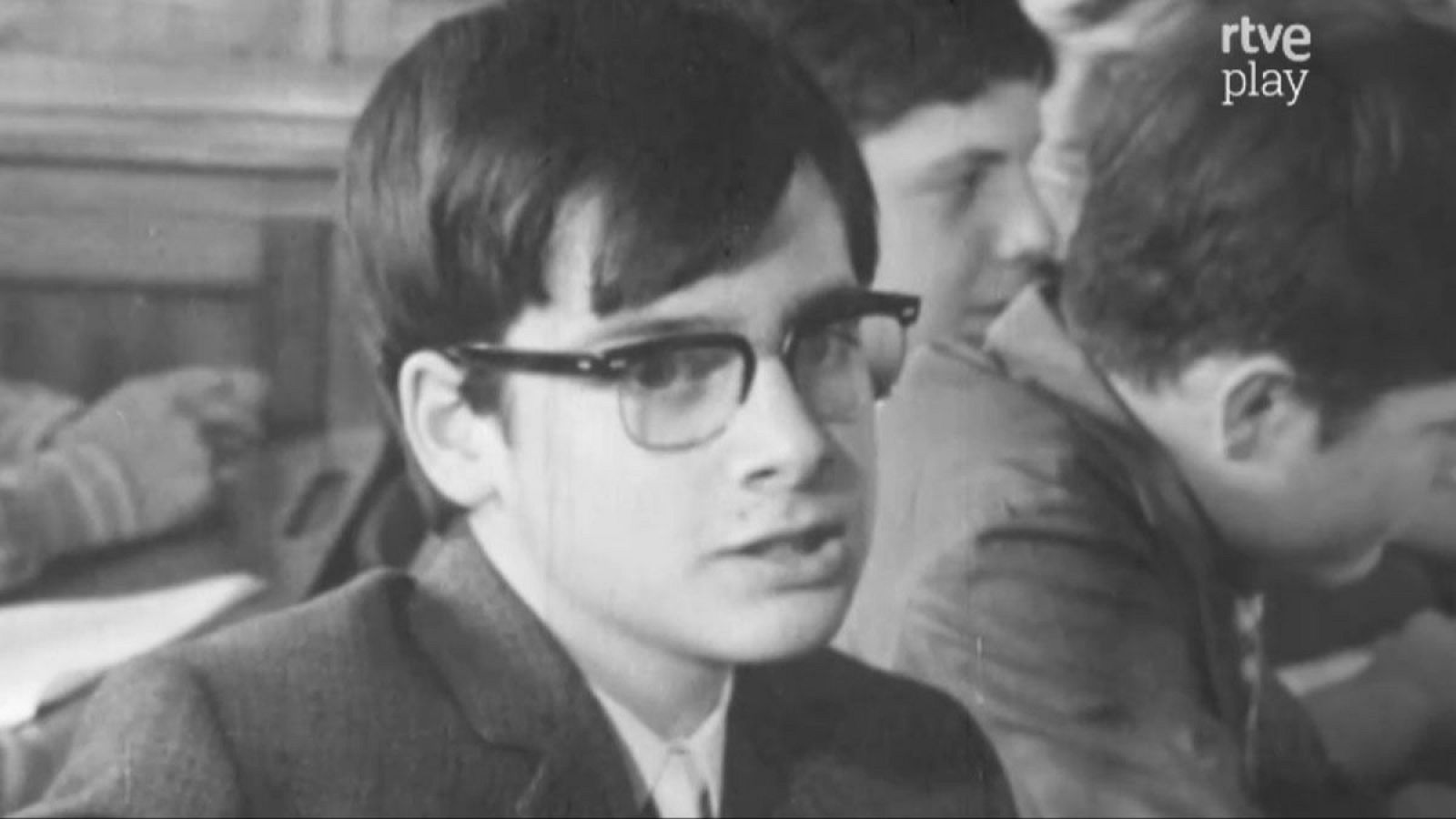 Joven estudiante con gafas oscuras y pelo peinado a un lado, en un aula. Imagen en blanco y negro con logo 'rtve play'.