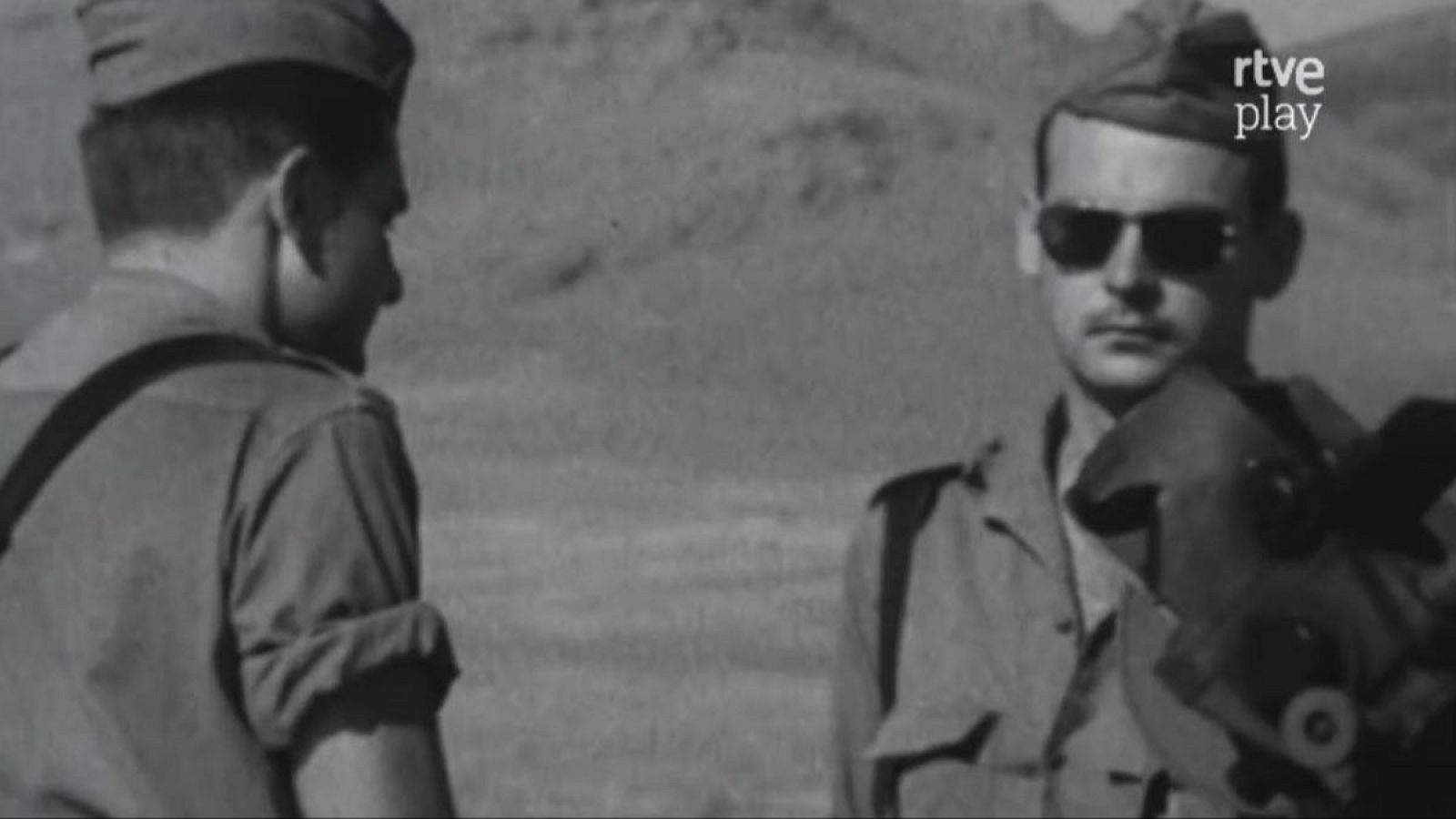 Soldados en un entorno árido, uno de frente con gafas de sol y el otro de espaldas. Fotografía histórica en blanco y negro con logo de RTVE Play.