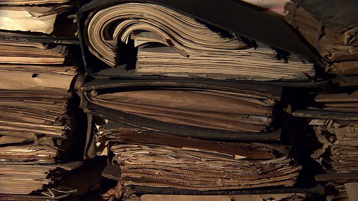 Una pila desordenada de documentos antiguos, con un tono amarillento, sugiere un archivo histórico. Algunos papeles están contenidos en carpetas, mientras que otros sobresalen, indicando un almacenamiento sin clasificar.