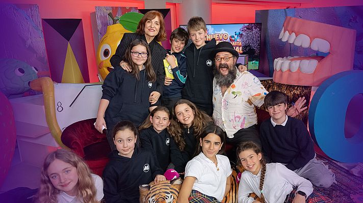 Elvira Lindo, rodeada de niños y un hombre, se encuentra en un set televisivo con decorados infantiles. La imagen anuncia un episodio del programa \"Un nuevo sendero hacia el manantial\", destacando el título \"La infancia con Elvira Lindo\".