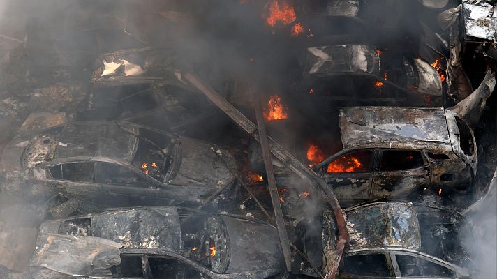 En Beirut, Líbano, tras un ataque, se aprecia una escena de destrucción con coches quemados y apilados, emanando humo negro y mostrando restos calcinados, evidenciando una destrucción generalizada.