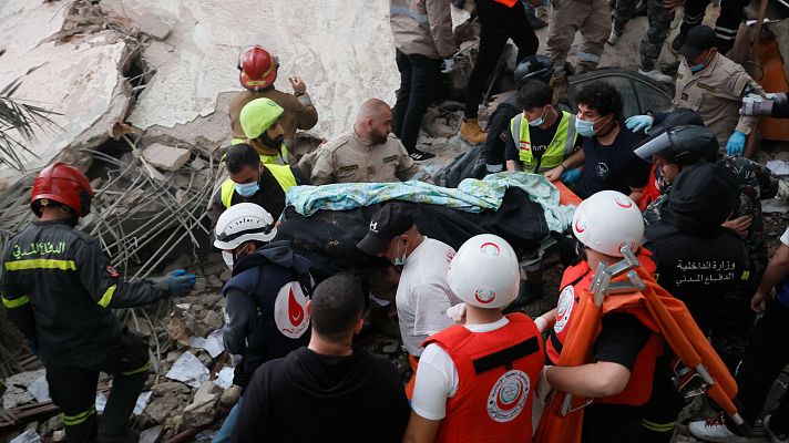 En Beirut, tras un ataque aéreo, rescatistas de la Defensa Civil Libanesa trabajan entre los escombros de un edificio residencial destruido, transportando el cuerpo de una víctima. La escena refleja la gravedad de la situación.