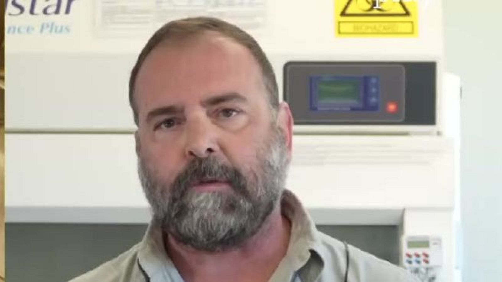 Primer plano de Juan José Luque en un laboratorio, con equipo científico, señal de biohazard y logo de TVE al fondo.
