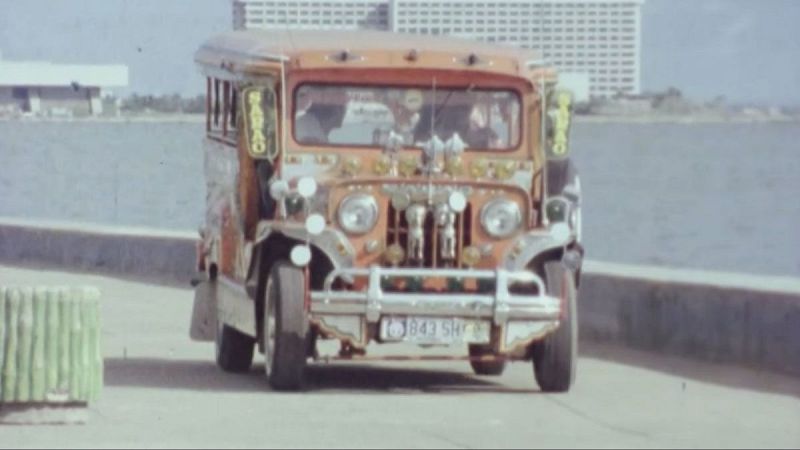 Jeepney decorado con cromados y luces en Manila, Filipinas. Matr�cula "J843 5H", cartel "SARAO". Carretera costera con edificios al fondo.
