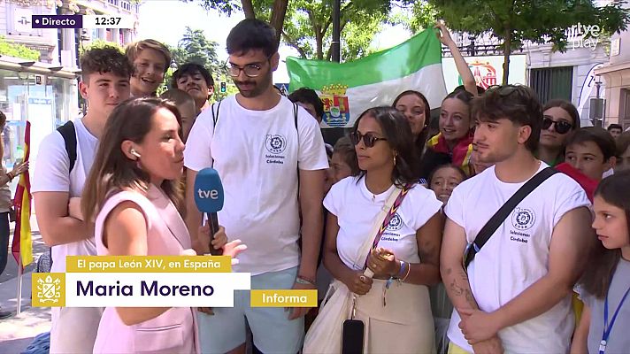 Reportera de RTVE, Maria Moreno, entrevista a jóvenes con camisetas de \"Salesianos Córdoba\" en un evento público con banderas de Andalucía y España.