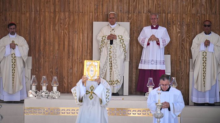 Papa Benedicto XVI preside una misa al aire libre, rodeado de clérigos. En primer plano, un sacerdote sostiene un objeto sagrado dorado.