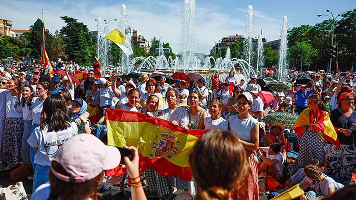 Multitud expectante en plaza de Madrid con banderas de España y Vaticano, esperando el paso del papa León XIV. Día soleado con sombrillas.