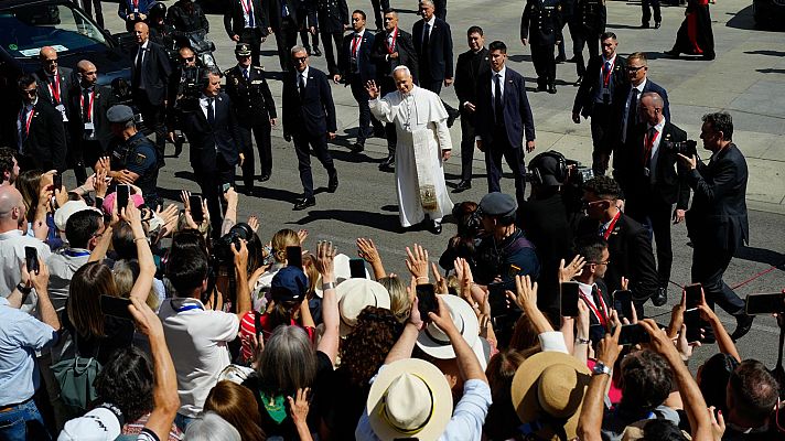 El Papa saluda a fieles en un evento al aire libre, rodeado de su séquito. La multitud, con móviles, documenta el momento bajo el sol.