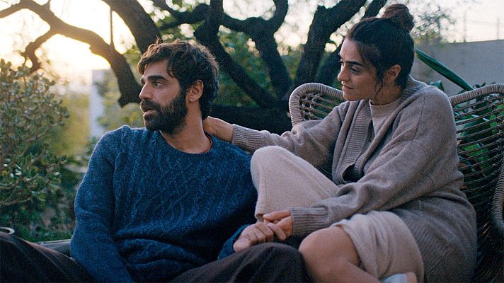 David Verdaguer y Lorena López en un jardín al atardecer. Él con jersey azul y barba, ella con cárdigan beige, comparten un gesto de cercanía.
