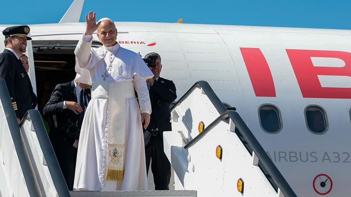 El Papa Francisco saluda desde las escaleras de embarque de un avión Airbus A320 de Iberia, acompañado por un piloto y otras personas, bajo un cielo azul.
