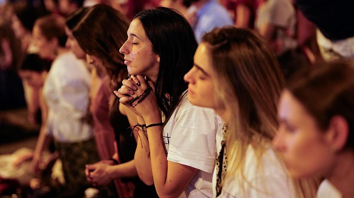 Jóvenes en profunda oración, una mujer con rosario en primer plano, rodeada de una multitud en un evento de recogimiento espiritual.