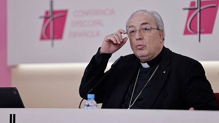 Primer plano de Francisco César García Magán, secretario general de la Conferencia Episcopal Española, con gafas y alzacuellos, hablando en un atril con el logo de la CEE detrás.