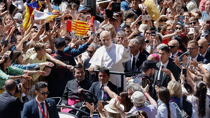 El Papa Francisco saluda a una multitud eufórica con banderas del Vaticano y de Cataluña/Aragón. Se observa personal de seguridad.