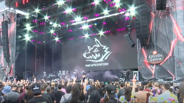 Escenario de concierto al aire libre con pantalla LED de \"MAN WITH A MISSION\", luces vibrantes, altavoces y una multitud eufórica. Se distingue el patrocinio de \"Estrella Galicia\".