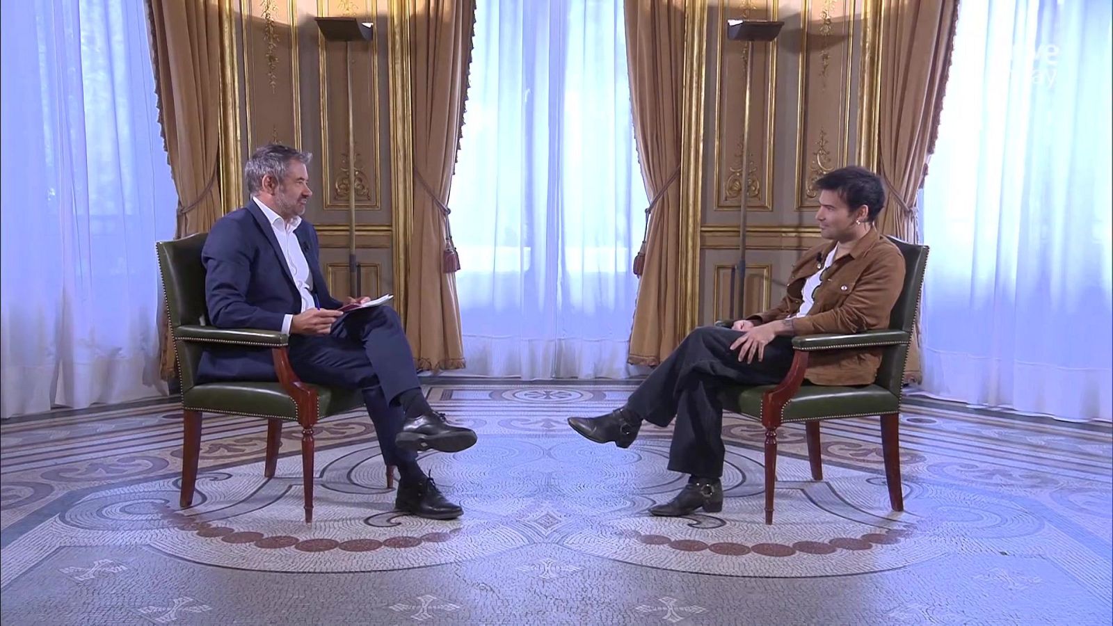 Javier del Pino y Dani Martín participan en un conversatorio en la Casa de América, sentados en butacas de cuero verde en un salón decorado.