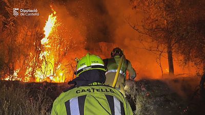 Bomberos de Castell�n luchan contra un incendio forestal nocturno. Un bombero con traje amarillo y casco "BMC 1428 Dr�ger" se ve de espaldas, mientras otro se acerca al fuego.
